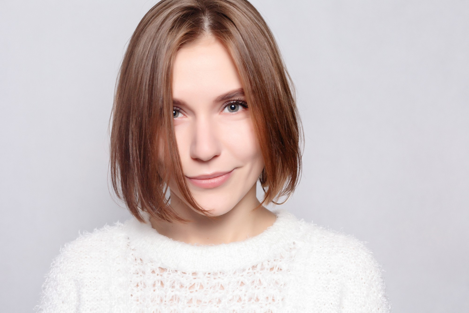jeune femme portant un pull blanc et qui pose devant un fond gris clair